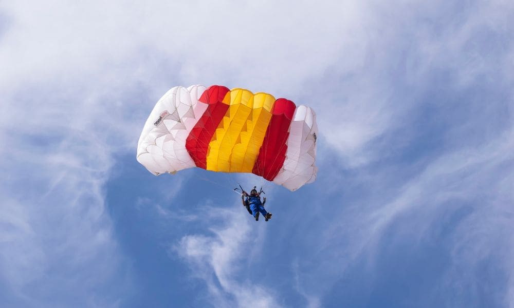 Ein Fallschirmspringer vor blauem Hintergrund mit weißer Bewölkung