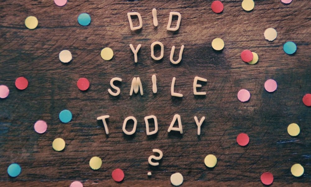 Die Worte "Did you smile today?" auf einem Holzhintergrund mit bunten Punkten